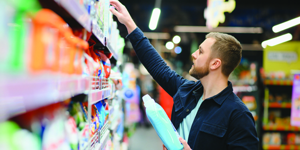 Man at the supermarket choosing a product from the shelf that looks like liquid laundry detergent.